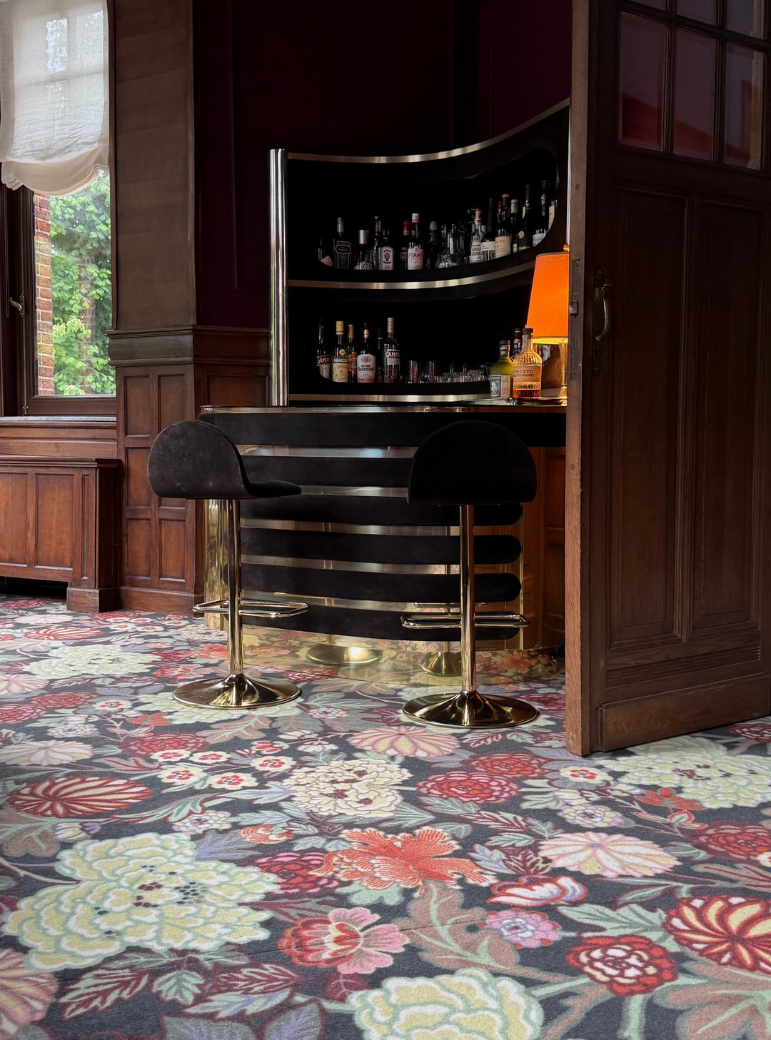 Tapijt met bloemenpatroon onder een huisbar met messing krukken