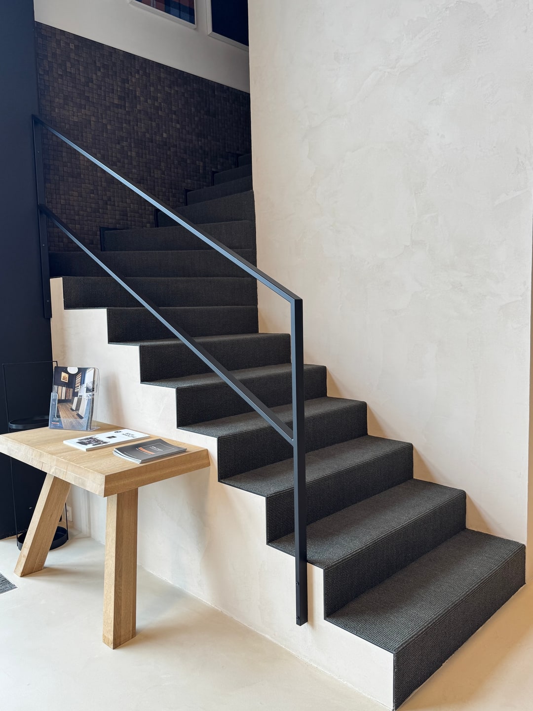 Rechte trap in antraciet tapijt met zwarte stalen leuning in onze showroom