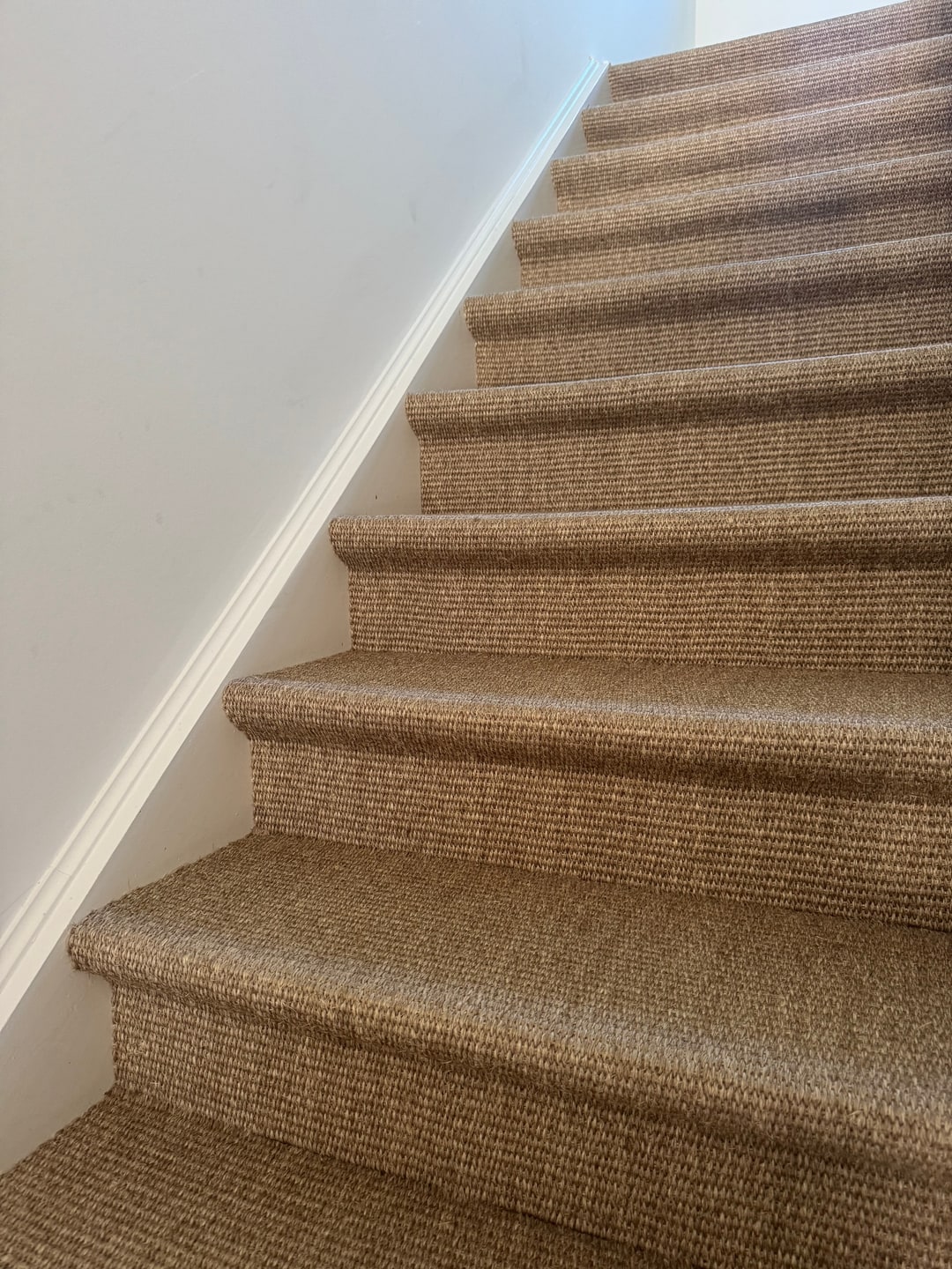 Opgaande trap in naturel sisal-look bouclé tapijt langs een witte wand