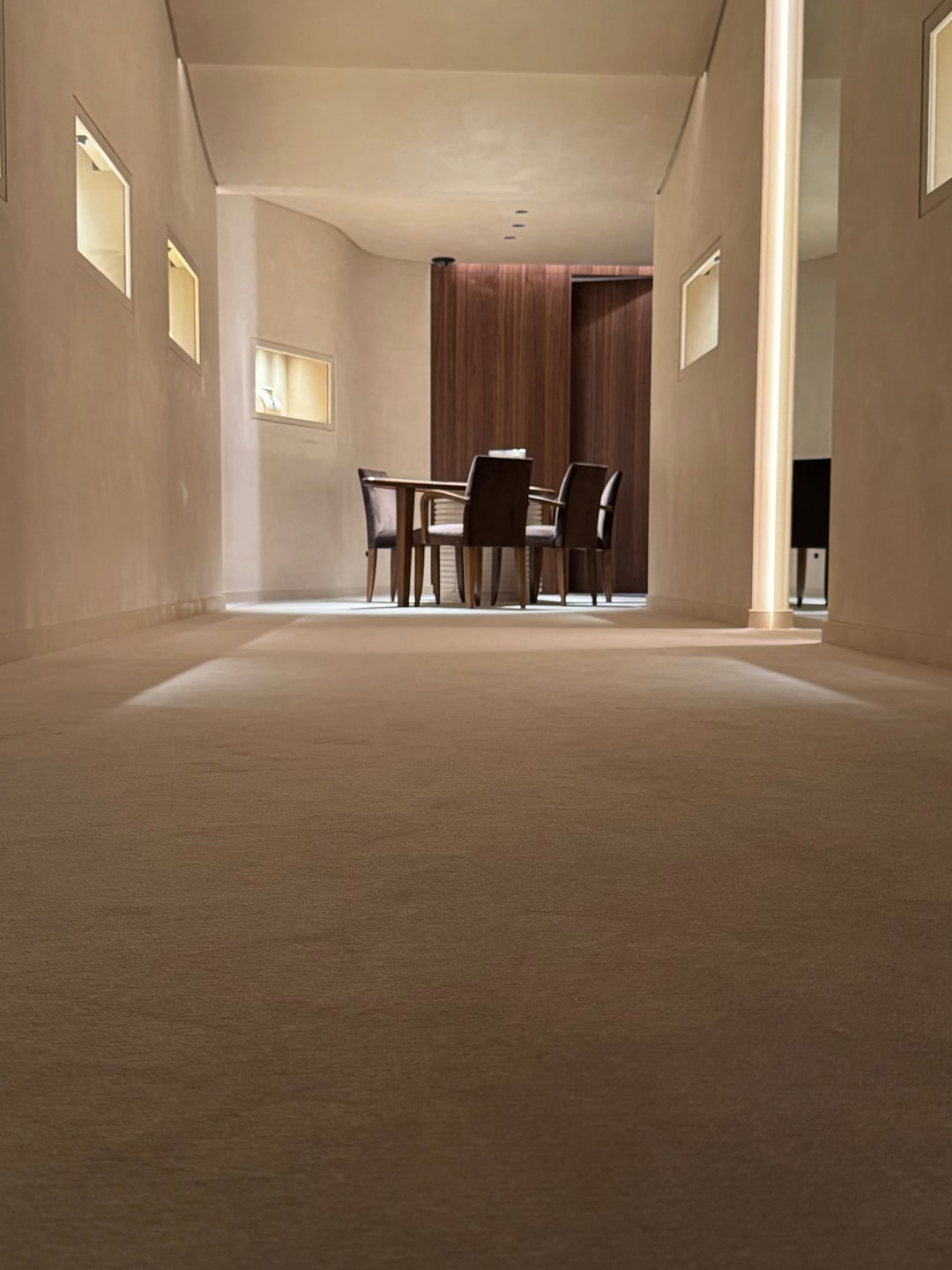 Egaal beige vasttapijt richting een tafel met velours stoelen, gezien vanaf de vloer